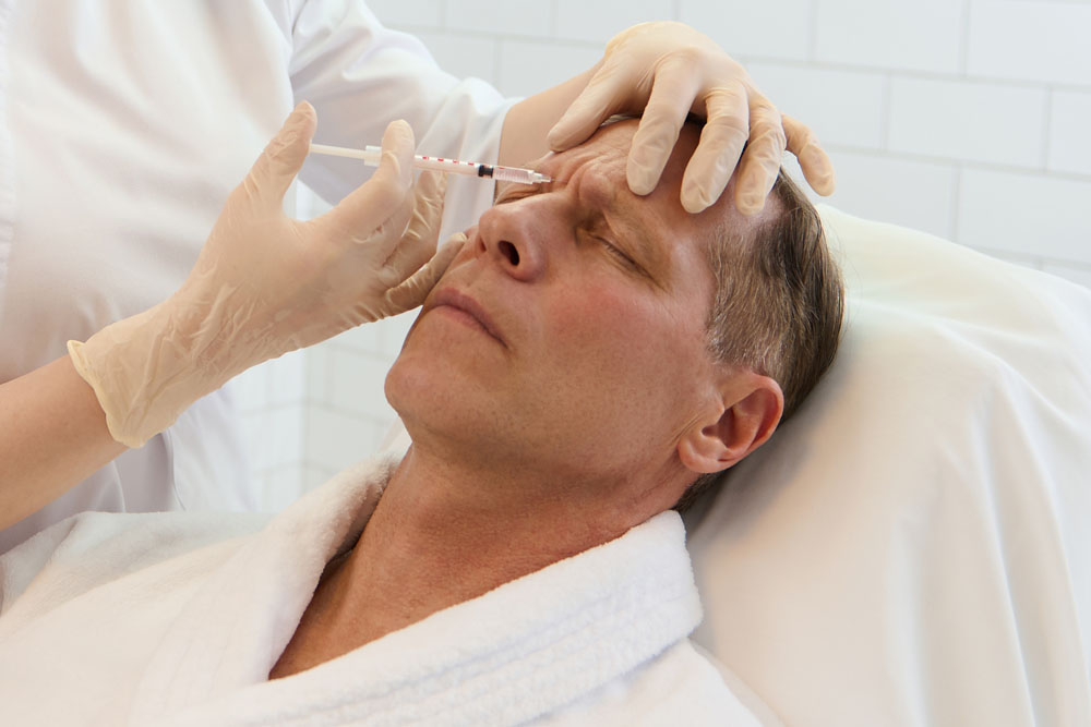 Portrait of smiling latin woman applying cream on her face while looking in mirror in her bathroom. Young multiethnic woman applying moisturizer on her cheek while looking in the mirror.
